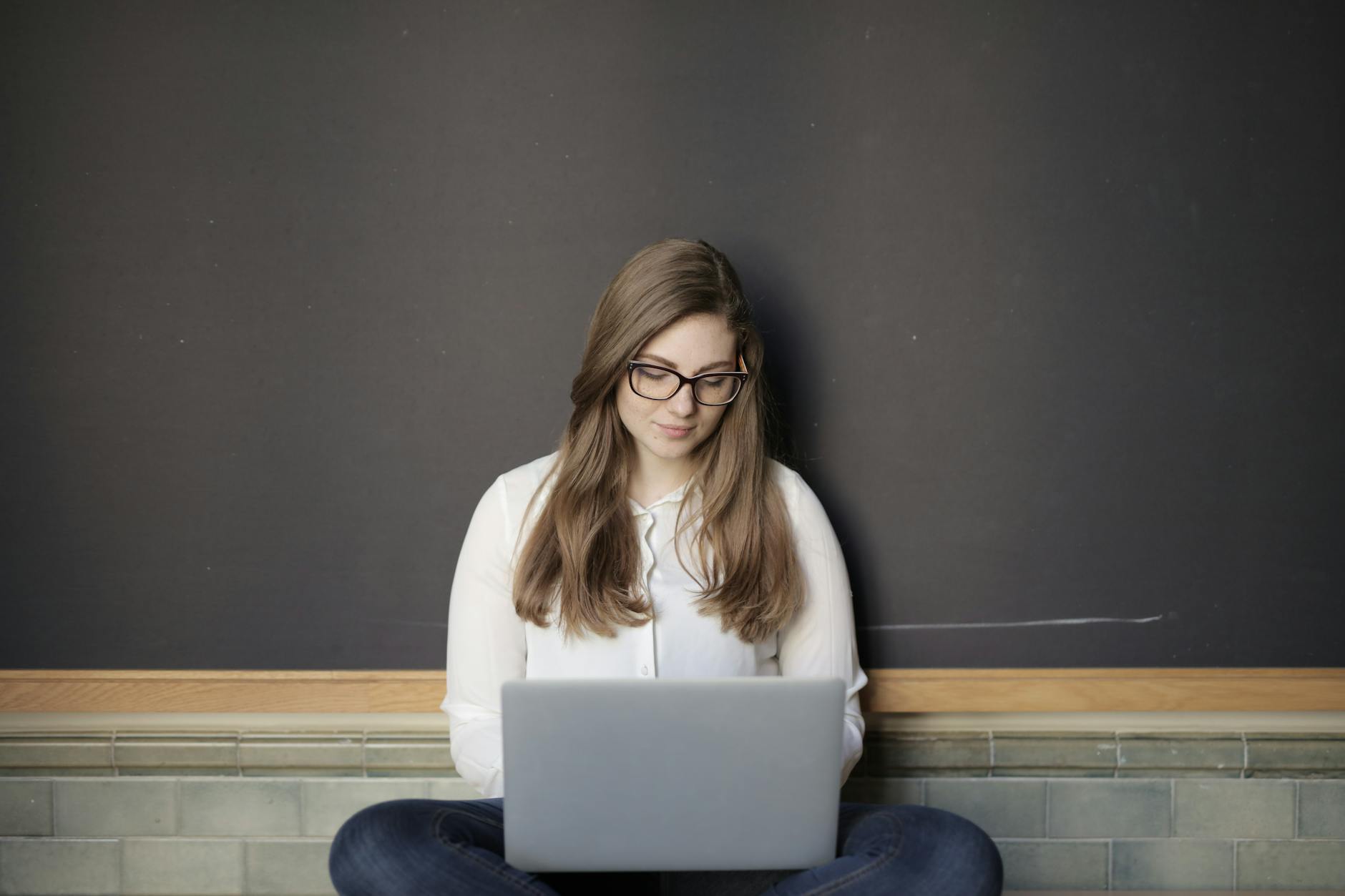 woman in white long sleeve shirt and blue denim jeans while using macbook