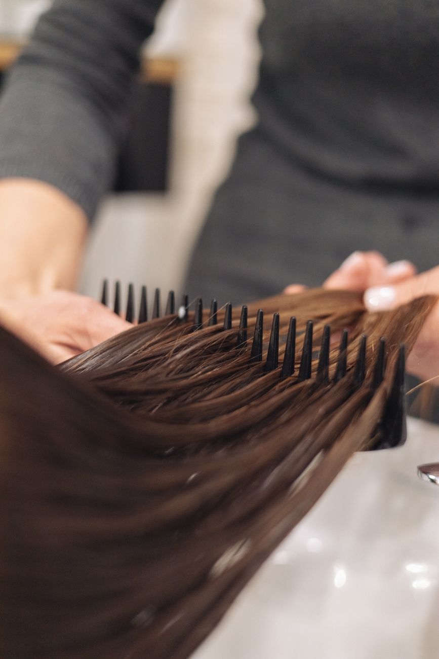 Experience the Bounce: Transforming Lifeless Locks Today 1 a hairdresser combing clients hair