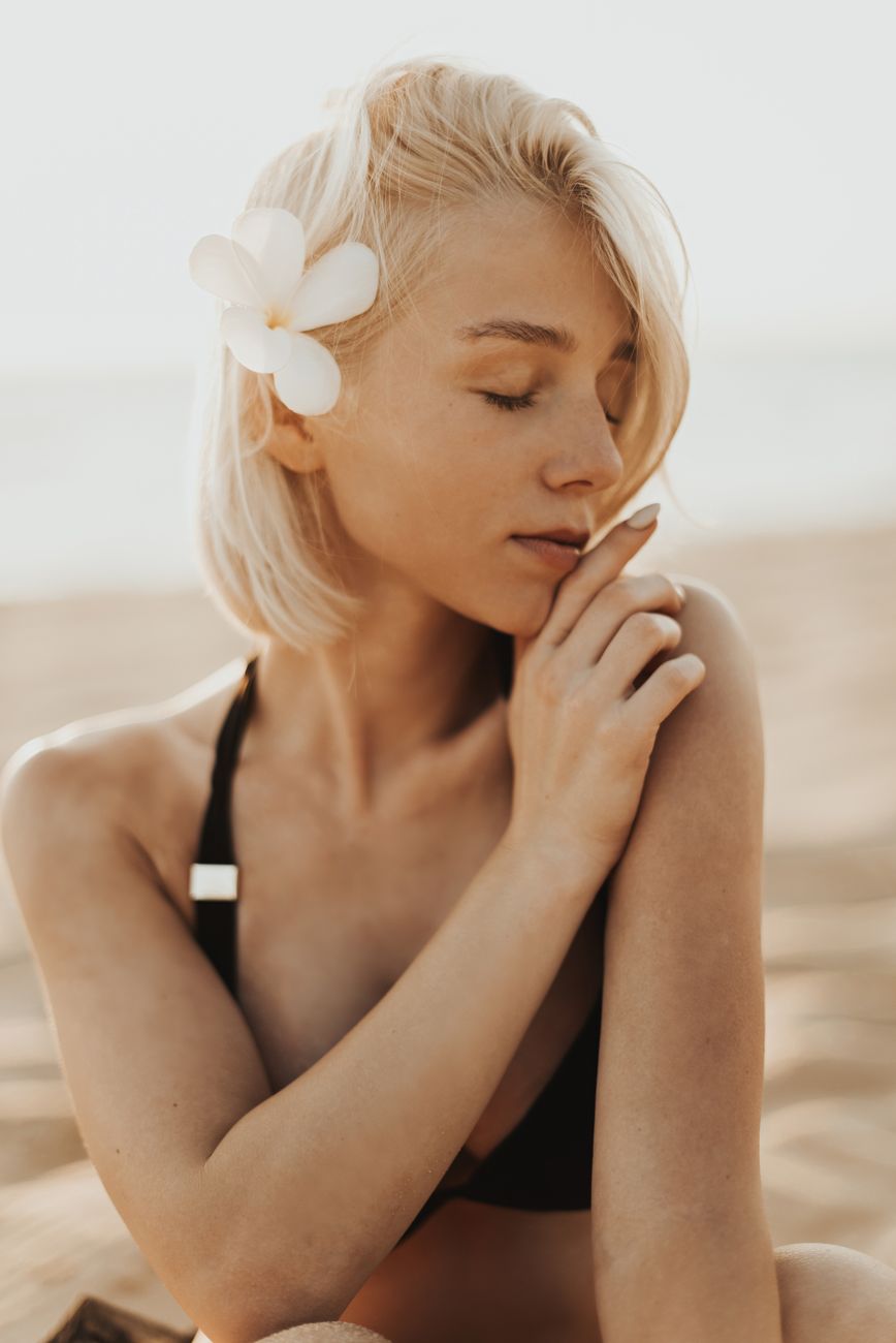 Beach Wood Blonde: The Ultimate Lived-In Summer Color 1 woman in black swimwear with flower on her ear