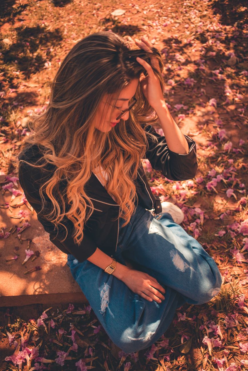 a woman in black jacket and blue denim jeans sitting on brown rock