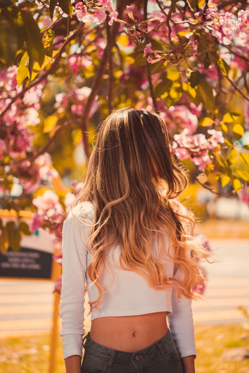 woman in white long sleeve shirt standing near pink flower tree