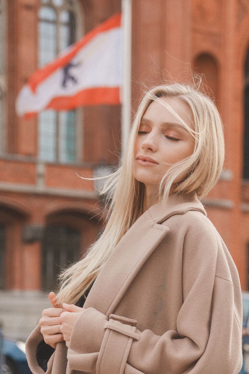 Warm Vanilla Balayage for Medium-Length Hair 1 portrait of blonde woman wearing coat on a street in germany