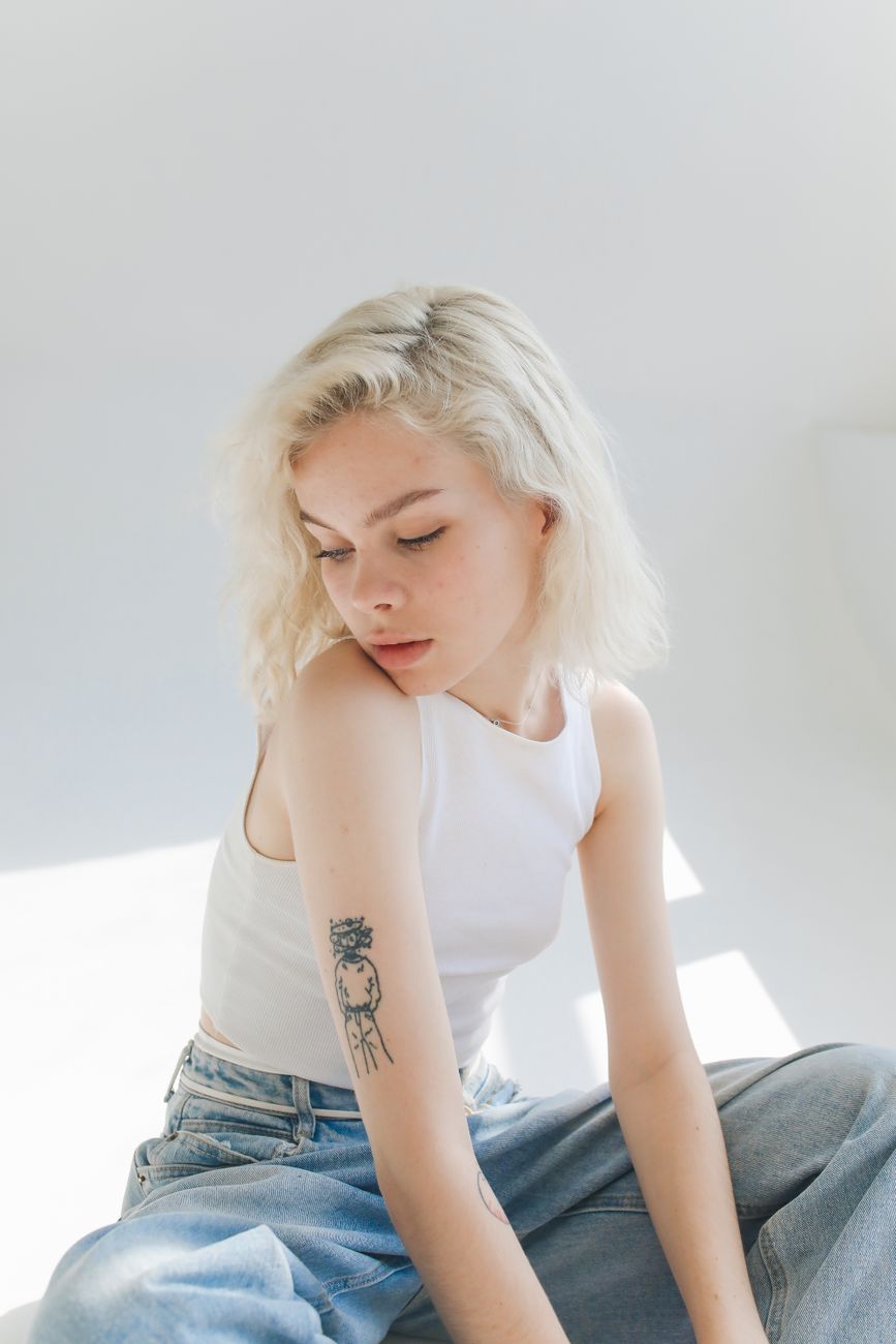 Going Platinum: What to Expect During Your Blonding Journey 1 young woman in a white top and jeans sitting in a bright room