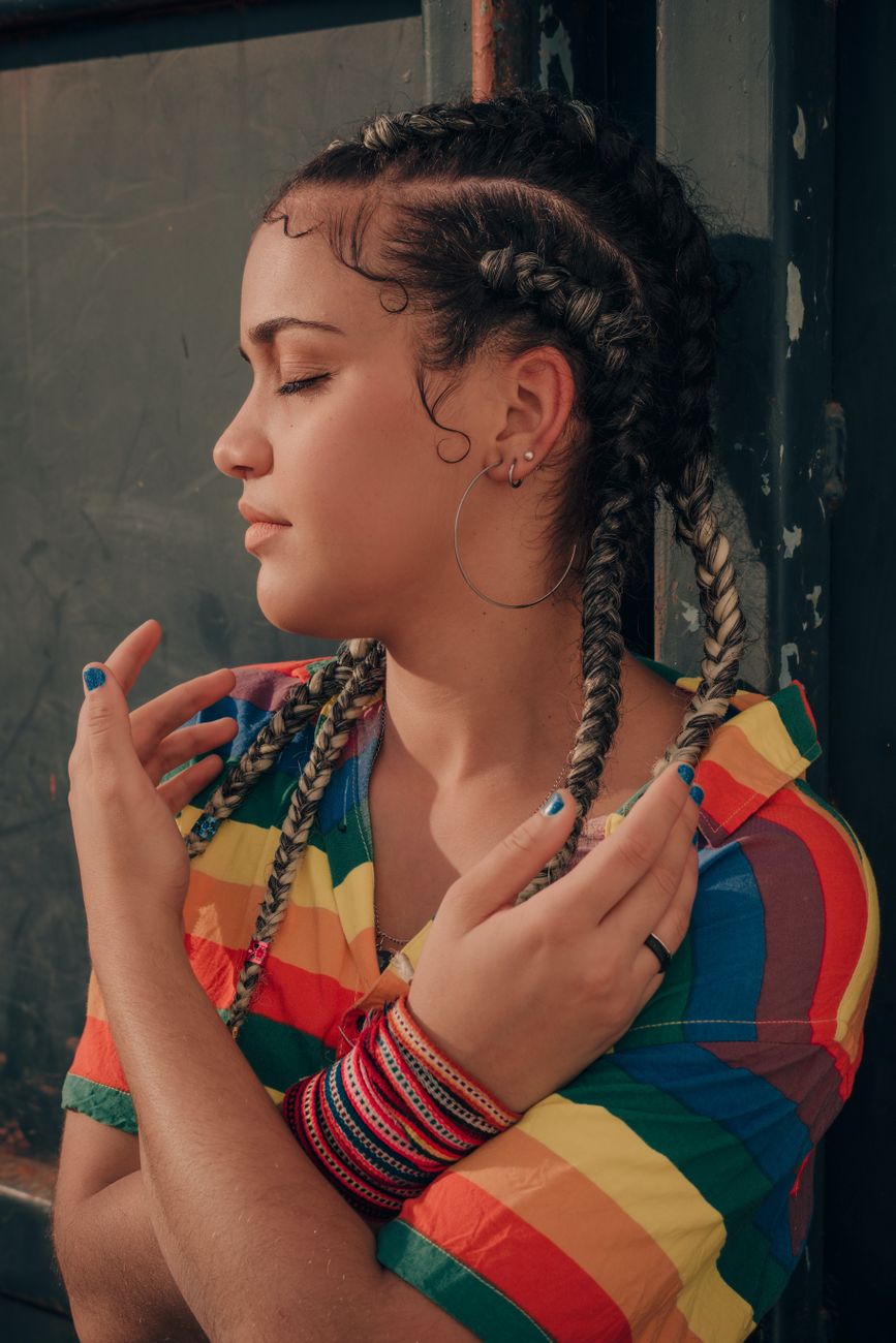 Summer Festival Braids with Colorful Extensions 1 a woman in braided hair wearing colorful top leaning on the wall while eyes are closed