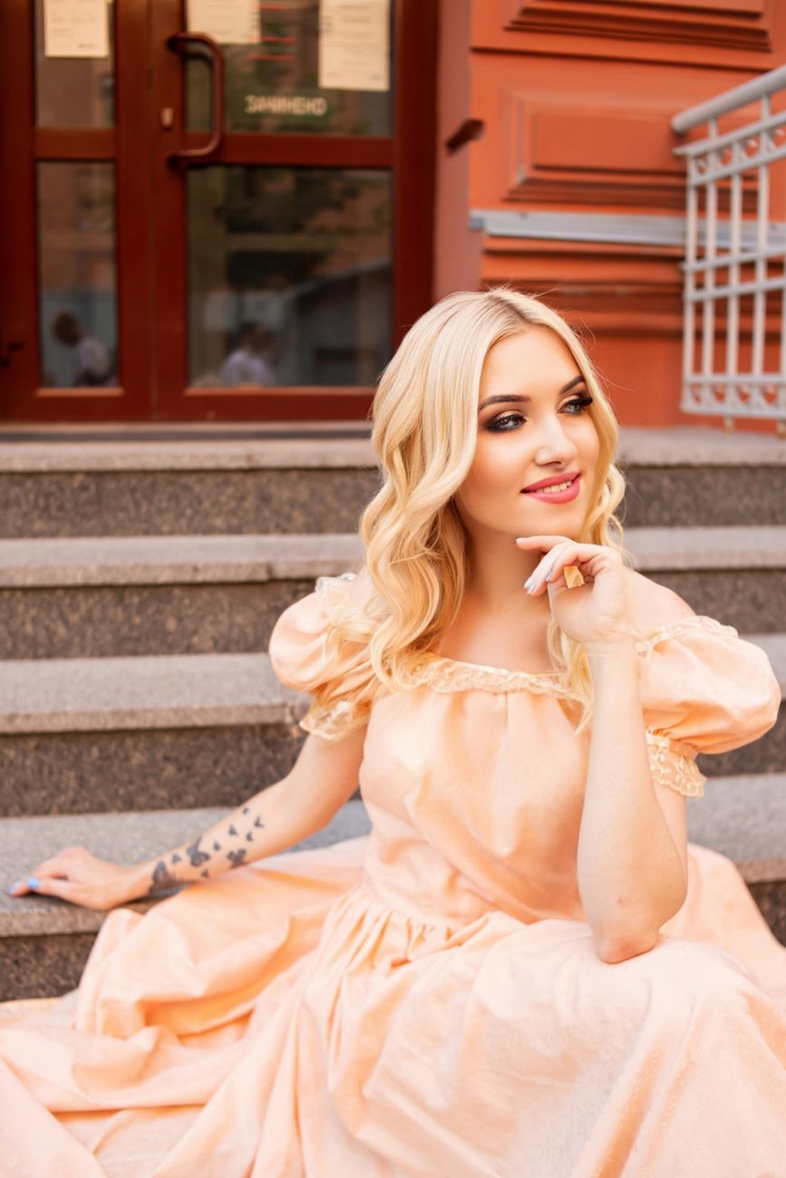 Pastel Peach Hair Color: Warm Soft Tone Inspiration 1 a blonde woman in a peach dress sitting on steps