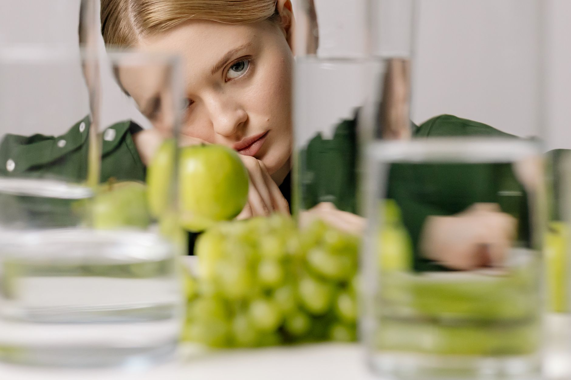 The Connection Between Diet, Hydration, and Scalp Health 1 woman in green long sleeves near green fruits and glasses of water while seriously looking at the camera